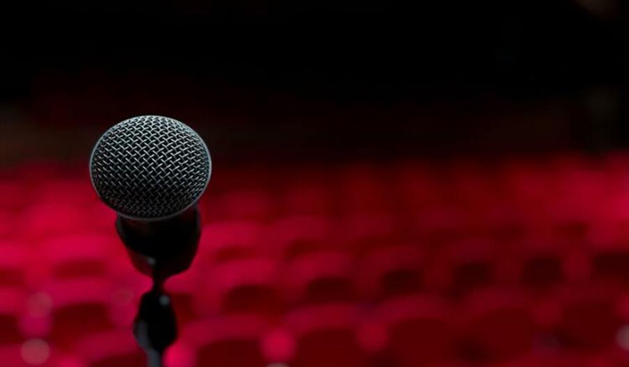 A microphone on a stage in front of red theatre seating