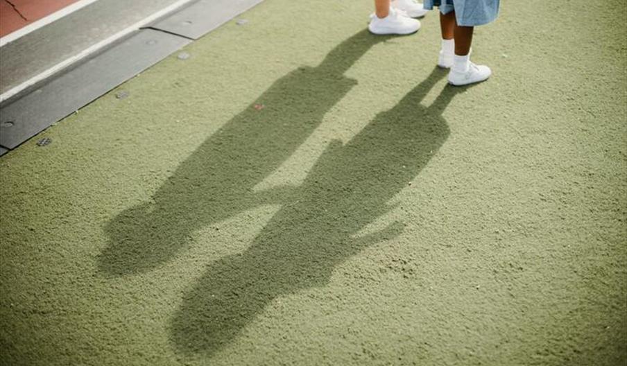 Two children casting shadows on a green surface