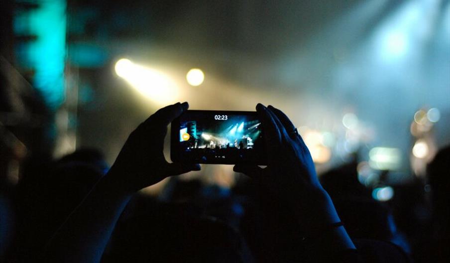 Hands holding a mobile phone taking a picture at a concert