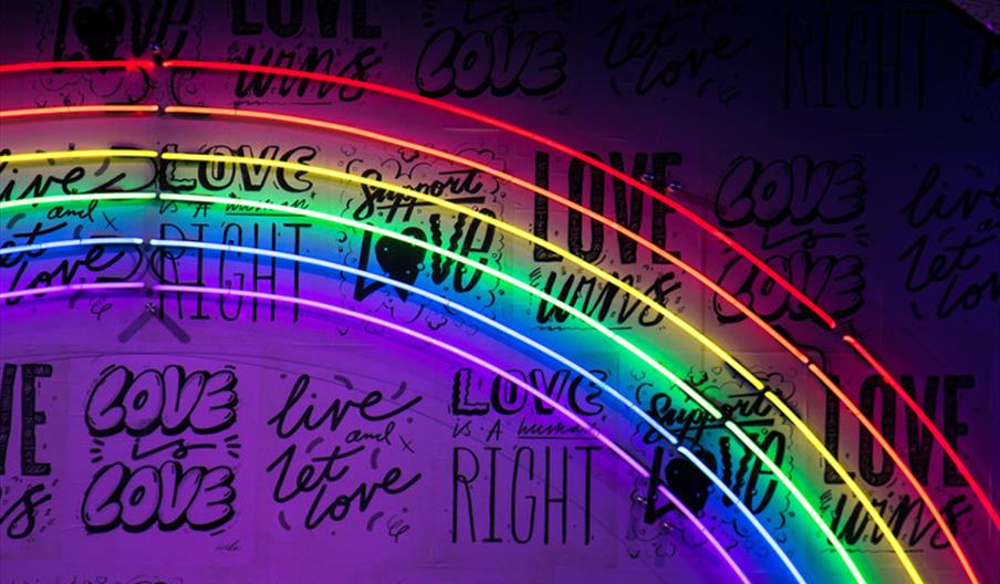 A neon rainbow sign with black writing behind it