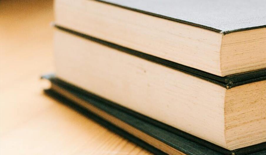 Close-up image of stack of hardcover books on a wooden table