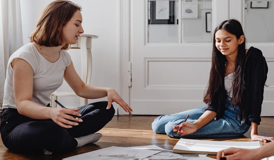 Two people sat on the floor between art supplies