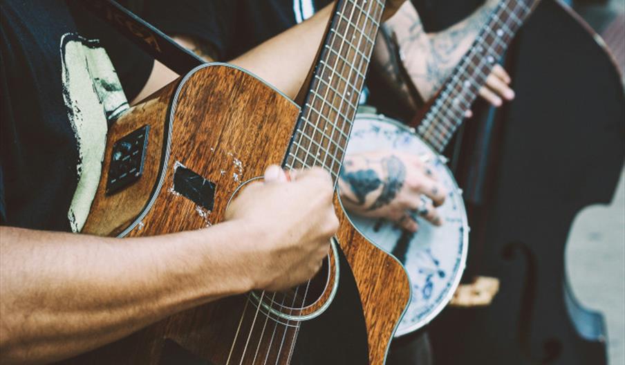 Person playing a banjo and another playing a dark wood acoustic guitar and another with a double bass