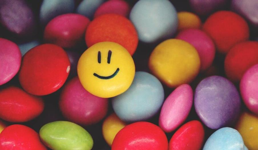 Multi-coloured candy with one yellow smiley faced candy on top