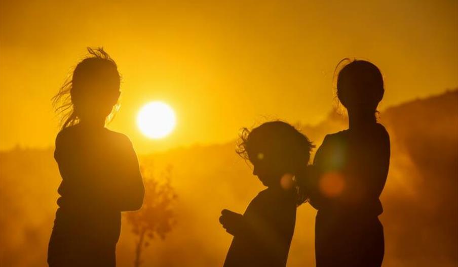 Three children silhouetted against a vibrant sunset